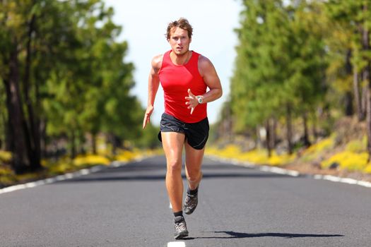 Running fitness sport man. Male runner sprinting on road - fit muscular male model training for marathon running fast on beautiful road in nature.