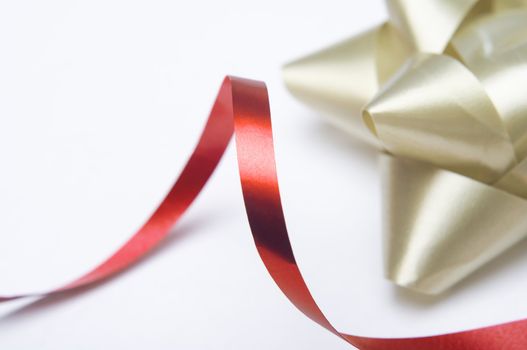 Close of of a swirling red ribbon with a gold decorative rosette in the background.  Shallow depth of field.  White background provides copy space.