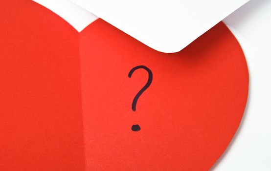 Close up of a red, heart-shaped valentine's card, opened to reveal a hand written question mark.  Resting on top of a white envelope with it's flap overlapping the heart.  Copy space provided.