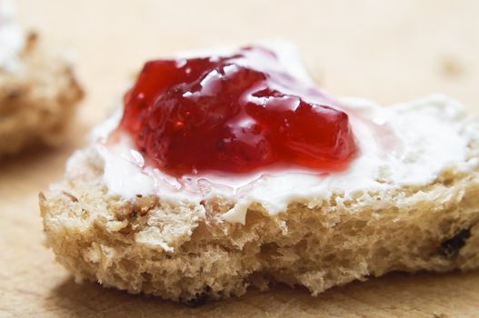 A heart shaped piece of bread topped with cream cheese and strawberry jam on a wooden surface.