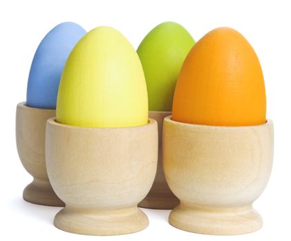 Close up of four hand-painted Easter craft eggs in unfinished wooden egg cups.  White background with light shadows.  