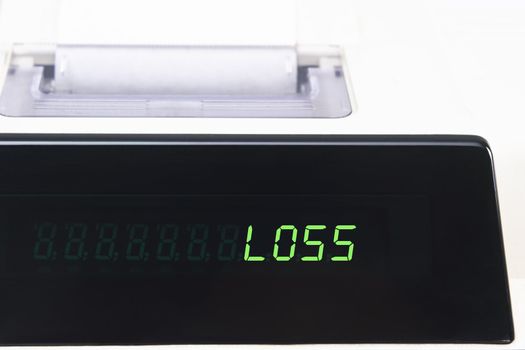 Close up of a calculator screen showing the word loss in bright green simulated LED.  Paper roll is visible in soft focus background.