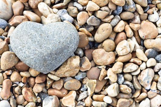 A grey heart shaped stone in upper left of frame, resting on a variety of smaller stones.  Landscape (horizontal) orientation.