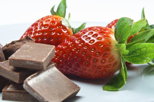 Close up of  a plate of strawberries, chocolate pieces and dusted truffles, with focus on the strawberries.