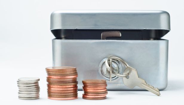 Close up side-view of stacks of coins in front of an open money box with key in lock.  The coins are British, but any visible embossing has been removed to enable generic usage.