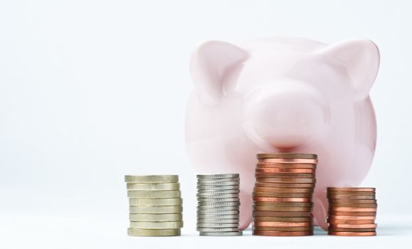 A pink piggy bank, facing front and looking over some coin stacks.  The coins used are British, but lettering has been removed to enable generic use.