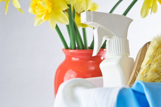 Horizontal shot of cleaning items in foreground with vase of daffodils in background to indicate Spring time.