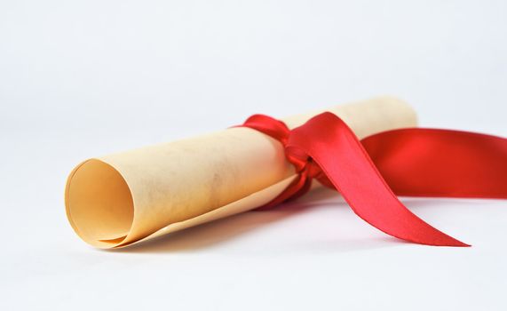 Close up of a rolled up diploma scroll, tied with a red ribbon.