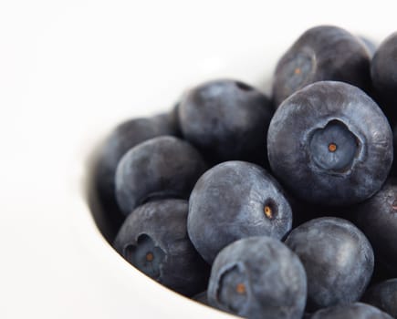 Close up (macro) of blueberries piled up in a white bowl.