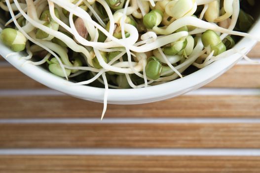 Overhead, cropped shot of a bowl of mung beansprouts, with horizontally slatted bamboo placemat in lower frame.