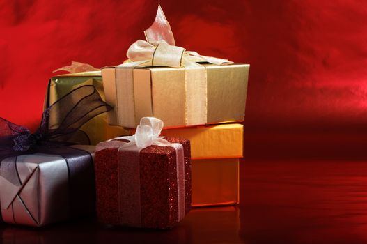 A selection of Christmas gifts, wrapped with tied ribbons against a metallic red background.  Copy space to right.  Horizontal (landscape) orientation.