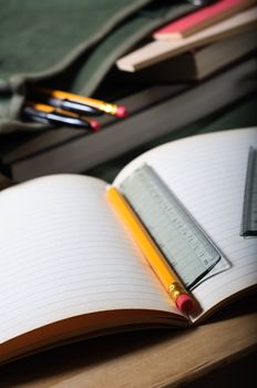 An open exercise book on table with pencil and ruler.  Open satchel in background.  Vertical (portrait) orientation.