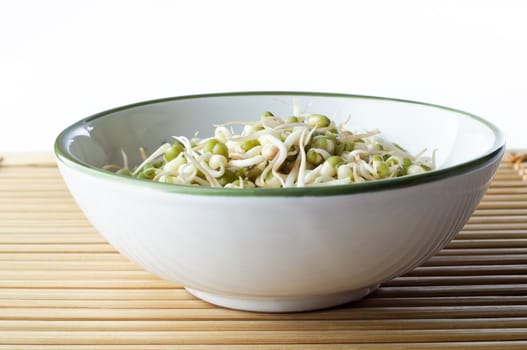 A bowl of mung beansprouts on a bamboo placemat with copy space above.  Landscape (horizontal) orientation.