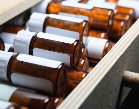 An open drawer, filled with many amber glass pill bottles containing homeopathic remedies.  Horizontal (landscape) orientation.