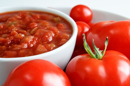 A white china bowl of red salsa, surrounded by fresh tomatoes.  Landscape (horizontal) orientation. 