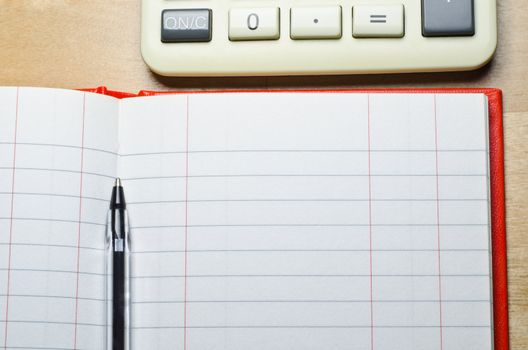 A calculator and an open, two column cash book with pen on a wooden desk.  Copy space is provided via empty leger (ledger) lines. Horizontal (landscape) orientation.