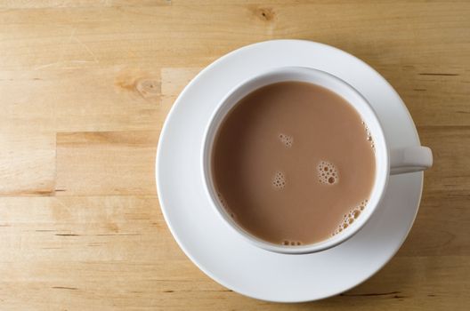 Overhead shot of a cup of tea, with saucer on old, scratched light wooden table with copy space to left.  Landscape (horizontal) orientation.