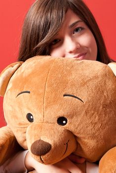 Young woman embracing teddy bear sitting close-up on red background