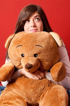 Young woman embracing teddy bear sitting close-up on red background