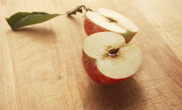 apple cut in half with stem and leaf on a cutting board