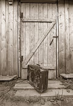 old valise near wooden door, sepia