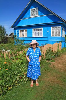 aging woman in blue robe near rural wooden building