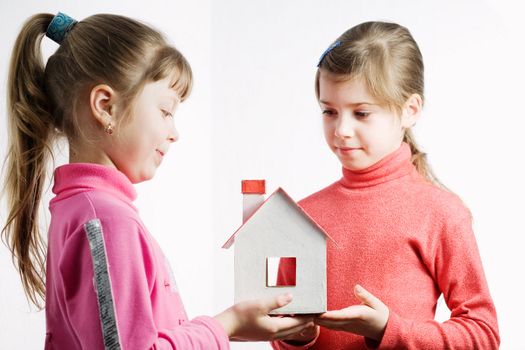 Two  pretty  little  girls  plaiyng  with a red and white doll's house made of plastic details

