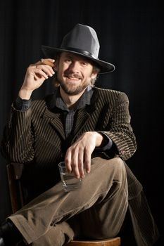 An image of a smiling man with cigar and glass