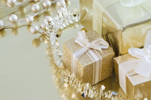 A collection of wrapped and tied Christmas gifts and decorations in gold shiny paper on reflective surface.