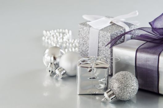 A collection of silver Christmas gifts and decorations on silver surface with soft sheen. Copy space to left. 