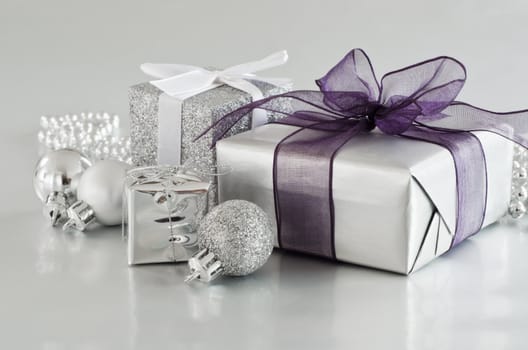 A selection of Christmas gifts and ornaments in silver, on a silver reflective surface.