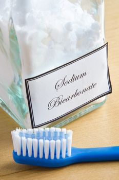 A bottle of sodium bicarbonate (baking soda) and a toothbrush on a wooden surface, to illustrate non-toxic dental care or natural toiletries.