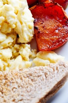 Close up (macro) of scrambled eggs and charred fried tomatoes with wholemeal toast on a white plate.