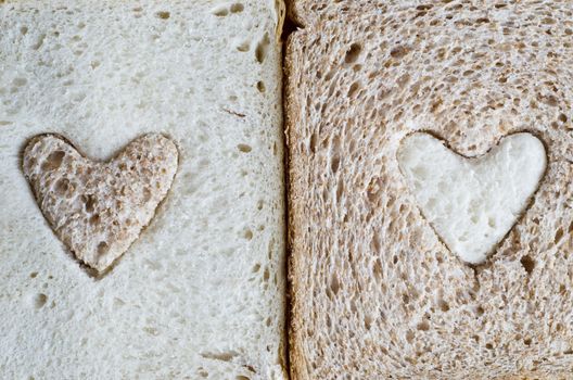 Close up of a white bread slice with a brown wholemeal heart, and a wholemeal bread slice with a white  heart.