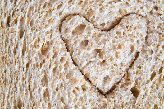 Close up (macro) of wholemeal bread with a heart shape cut into it, to illustrate love or a healthy heart diet.