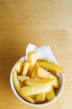 A bowl of chips (french fries) from above on a wooden table.  Copy space above.  Vertical (portrait) orientation.