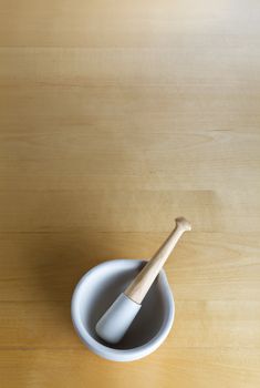 overhead shot of a pestle and mortar, centred lower frame on a wooden surface which provides generous copy space above.