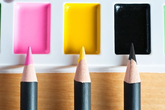 Close up of pencil tips pointing upwards to matching colours on a paint palette to illustrate colour matching or picking or mixed media.