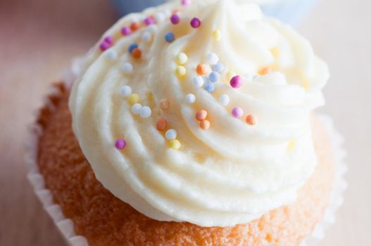 Close up ((macro) of a freshly baked cupcake decorated with a swirl of  buttercream icing and colourful  sprinkles.
