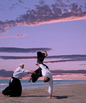 two adultes are training in aikido on a beach 