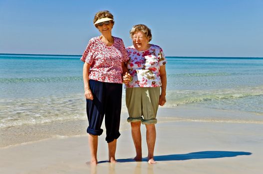 Two beautiful elderly women standing in the sand at the beach.