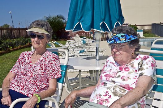 Two lovely women in their 80's sitting beside a pool.