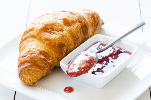 Croissant with raspberry jem on white wooden table