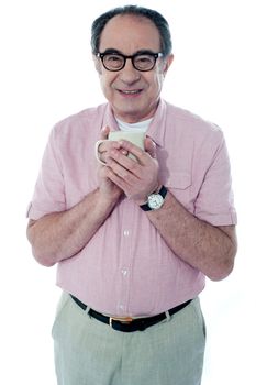 Smiling old man holding a coffee mug posing in front of camera