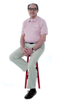Confident senior man looking at you as he rests on stool, studio shot