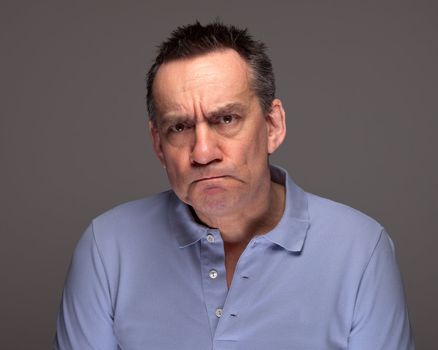 Handsome Middle Age Man Pulling Grimace Face and Glaring on Grey Background