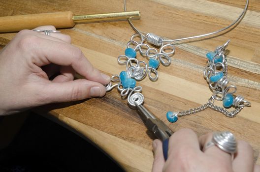 woman's hands creating a fashion jewelery with silver metal and turquoise gemstones