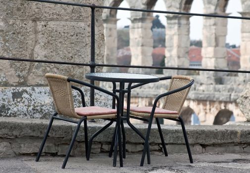 table and two chairs outdoor so close to roman amphitheater