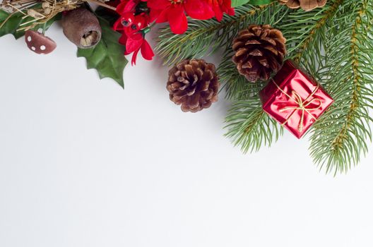 A Christmas themed border running from upper left to right side of frame, made up of a variety of artifical Winter flora decorations in greens, reds and browns, with a shiny tied gift box and real fir cones.