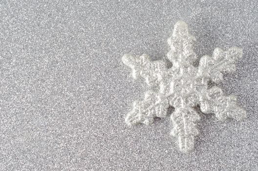 A sparkly silvery glitter encrusted snowflake on a silver glitter background.  Copy space to left.